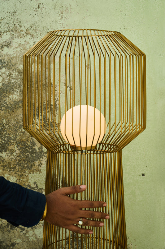 Gold cage-style lamp with a hand reaching towards it against a textured wall.
