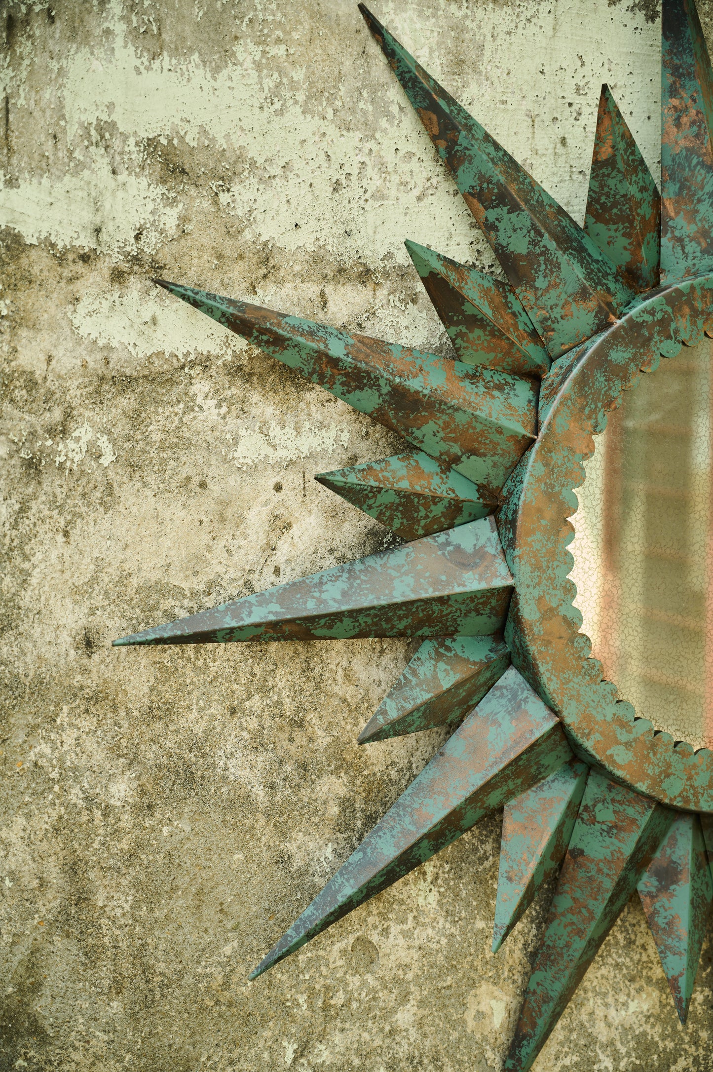 Decorative sun-shaped mirror with a textured surface on a concrete wall.
