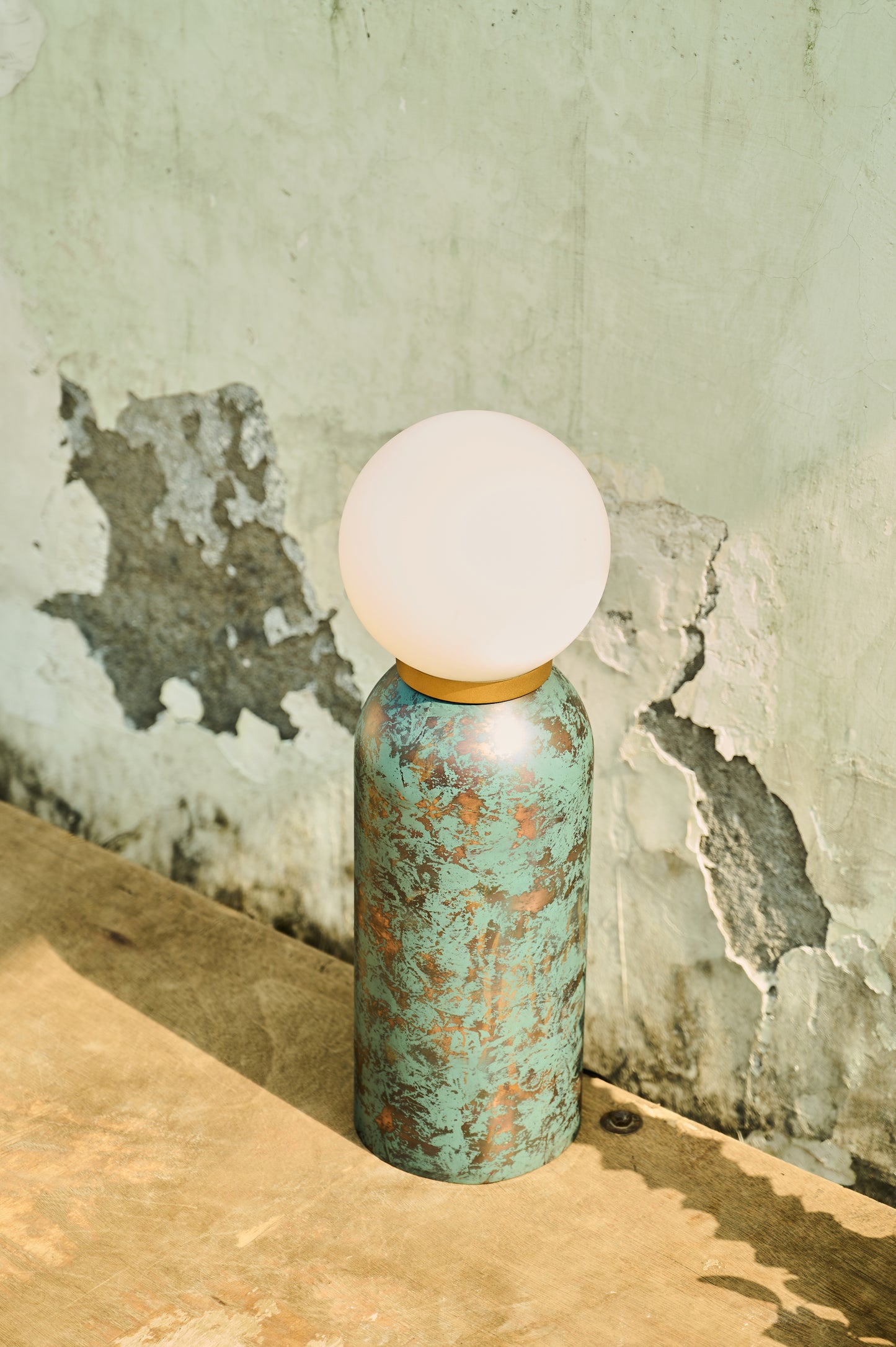 Table lamp with a textured green base and white bulb against a worn wall.