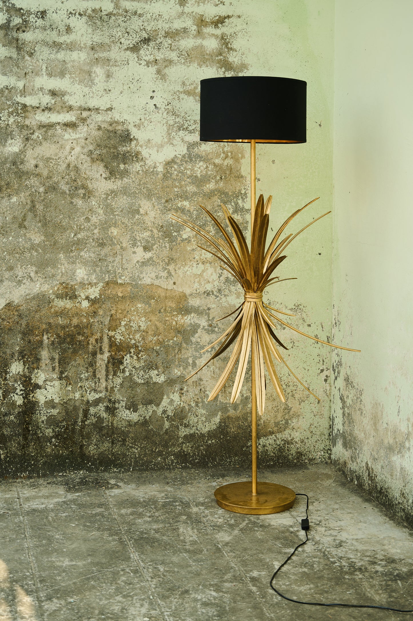 Floor lamp with gold base and black shade against a textured wall.