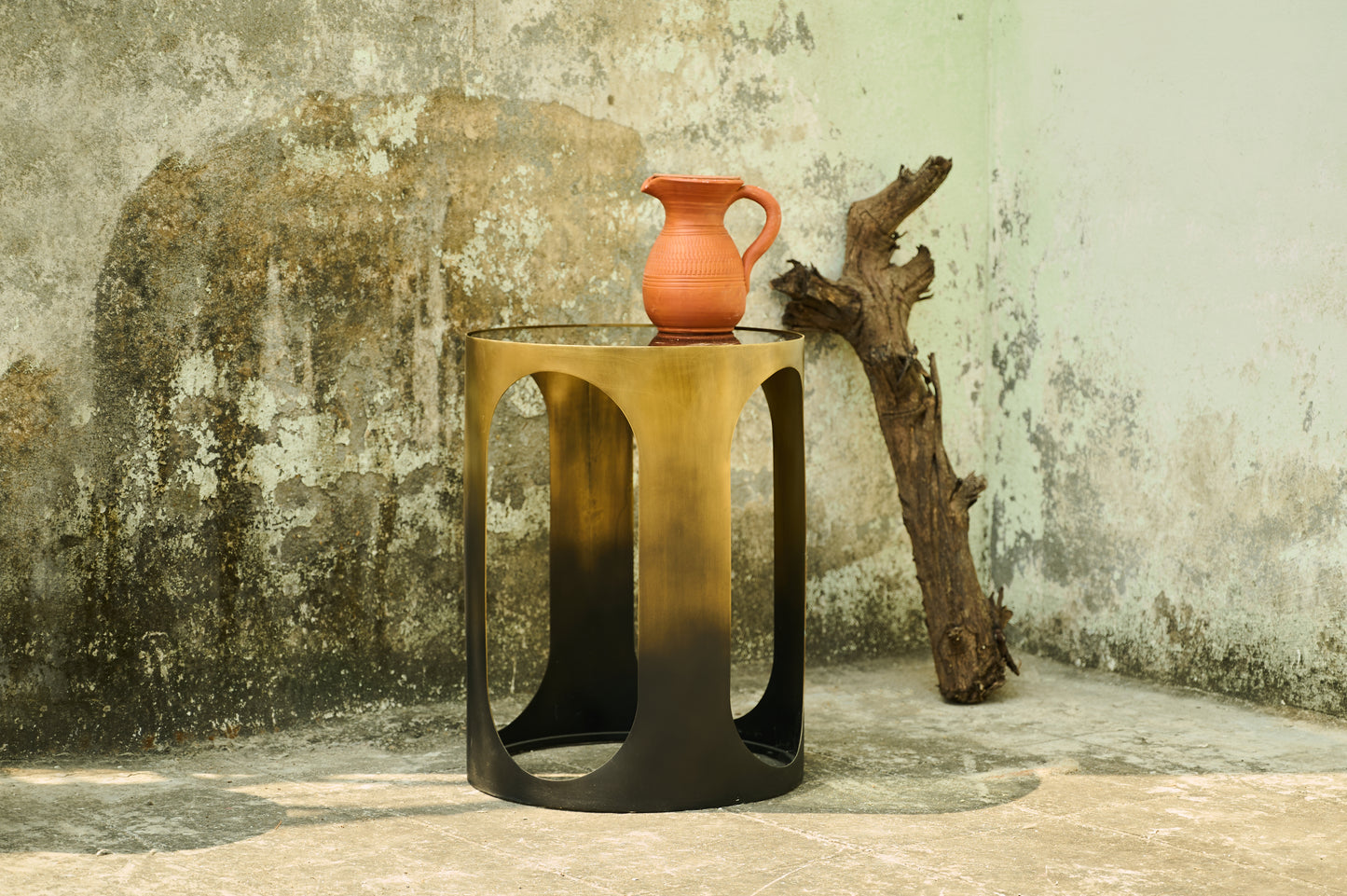 Small metallic table with a terracotta vase against a textured wall.