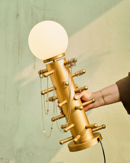 Gold lamp with a spherical bulb held by a hand against a light green background