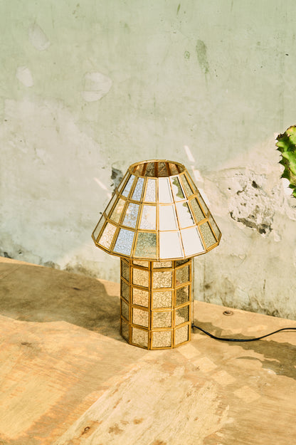 Decorative gold lamp with geometric design on a wooden surface against a textured wall.