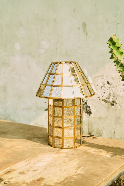 Decorative table lamp with glass shade on a wooden surface against a textured wall.