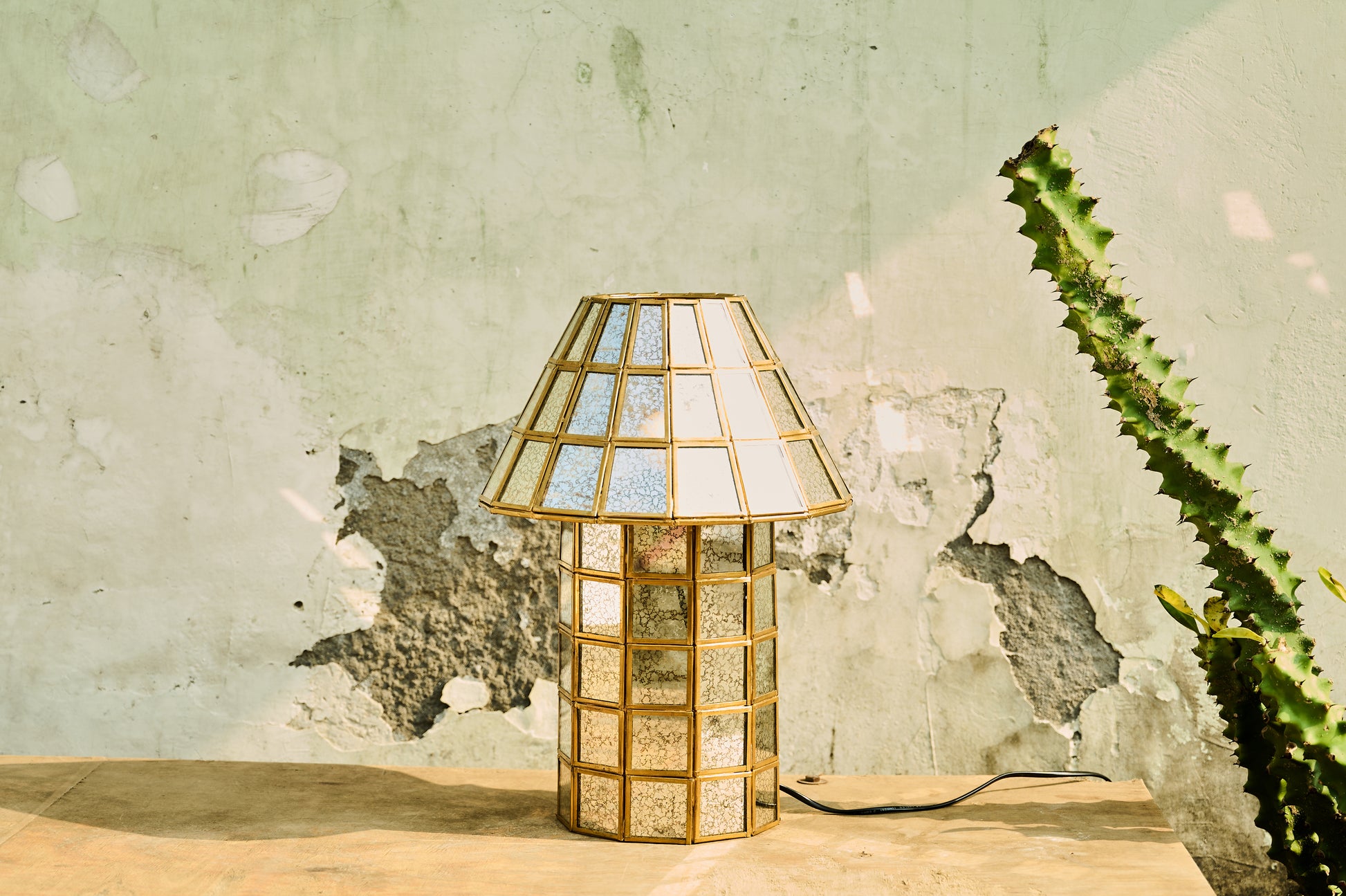 Decorative table lamp with a textured glass shade on a wooden surface against a textured wall.