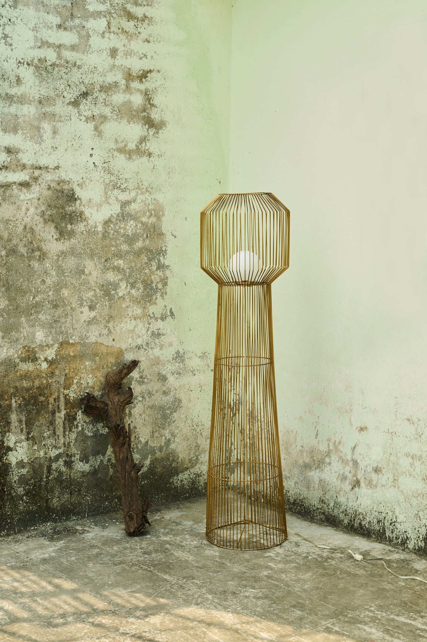 Tall wire cage floor lamp against a textured wall.