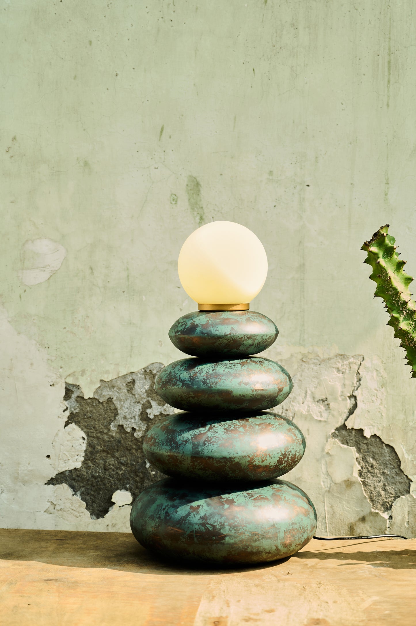 Stack of green stones with a light bulb on top against a textured wall.