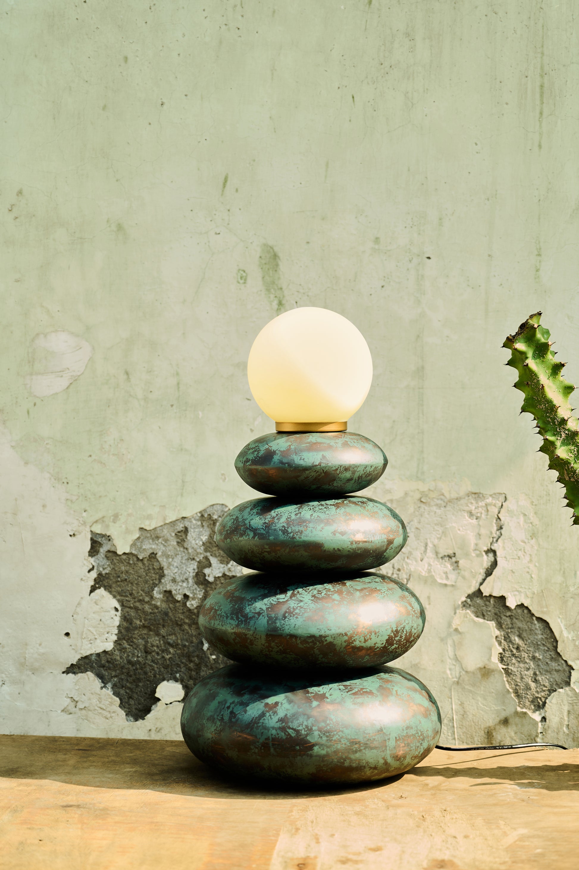 Stack of green stones with a light bulb on top against a textured wall.