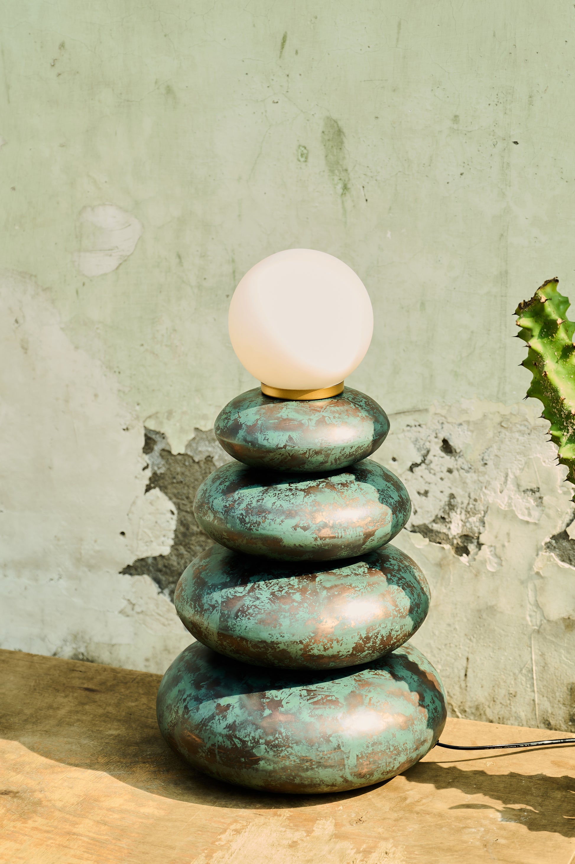 Stack of green stone-like lamps with a white bulb on top against a textured wall.