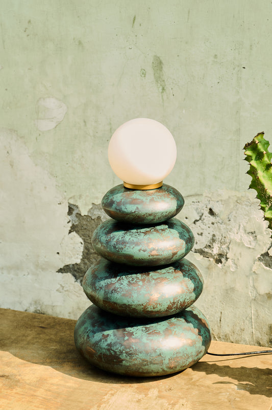 Stack of green stone-like lamps with a white bulb on top against a textured wall.