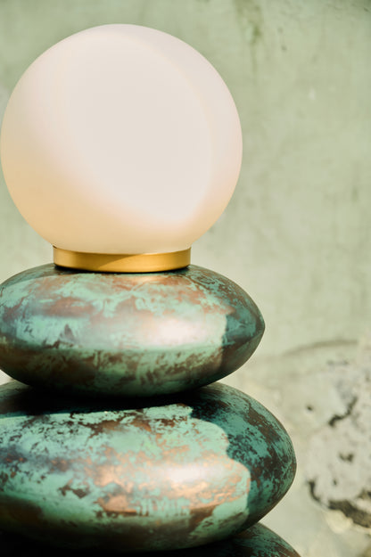 Table lamp with a green ceramic base and white glass shade on a textured surface.