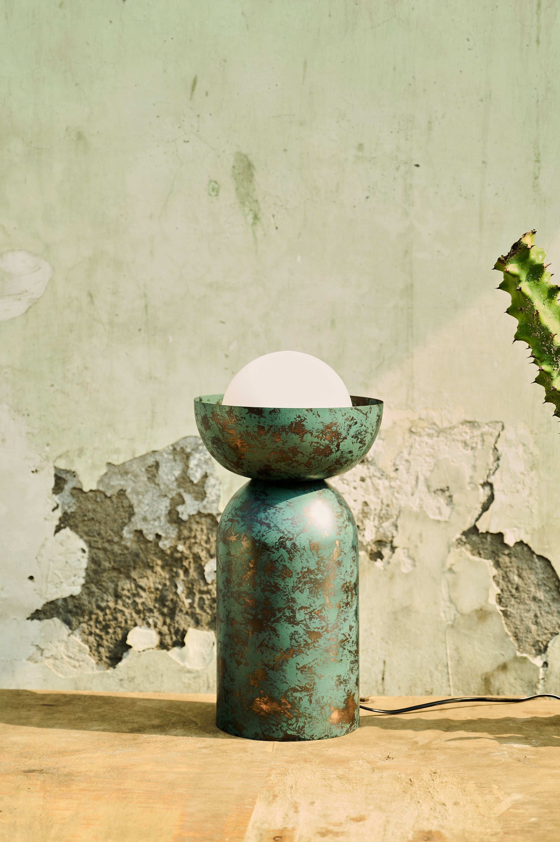 Green ceramic lamp with a white bulb on a wooden surface against a textured wall.
