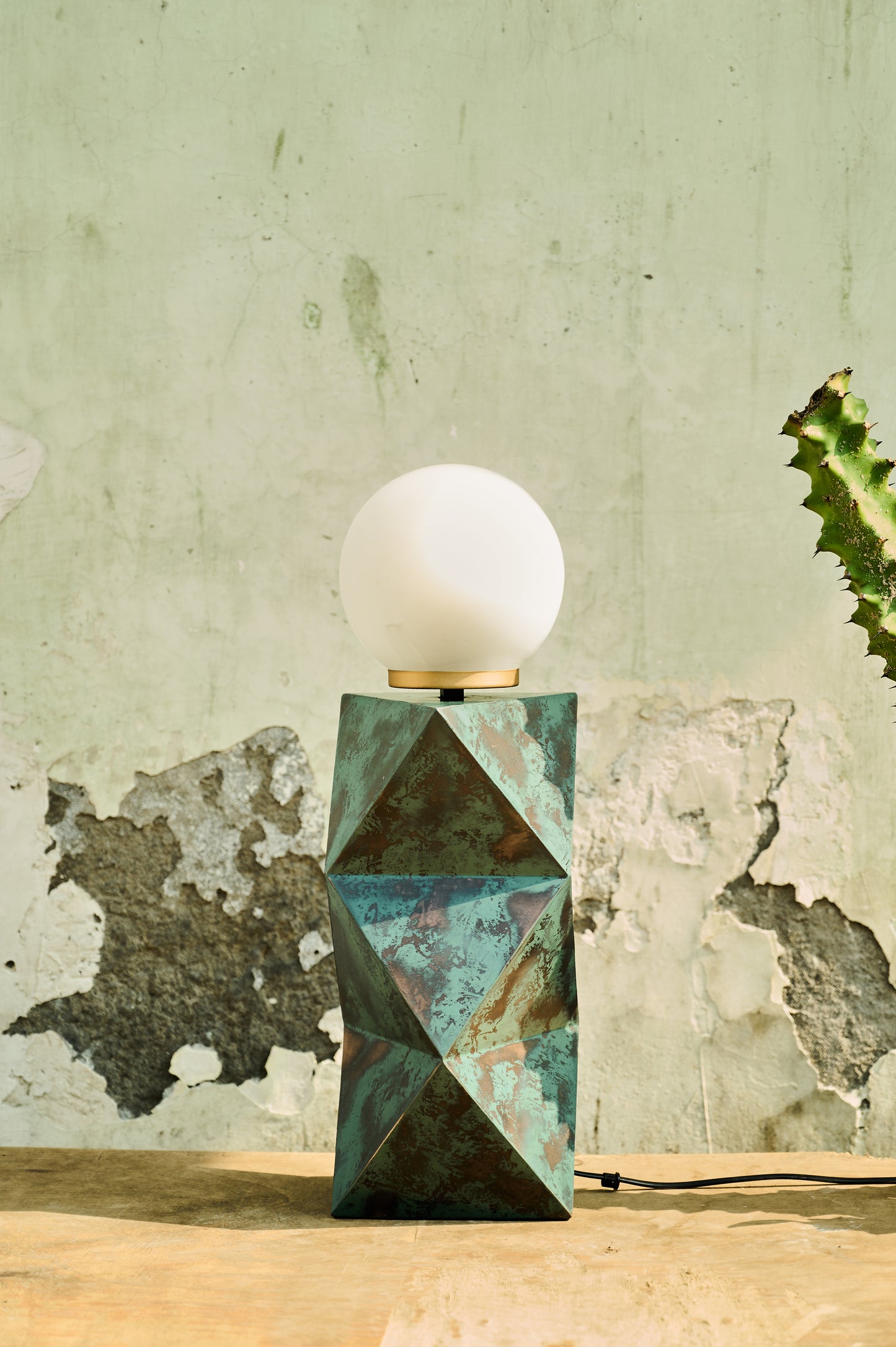 Table lamp with geometric base and white bulb against a textured wall.
