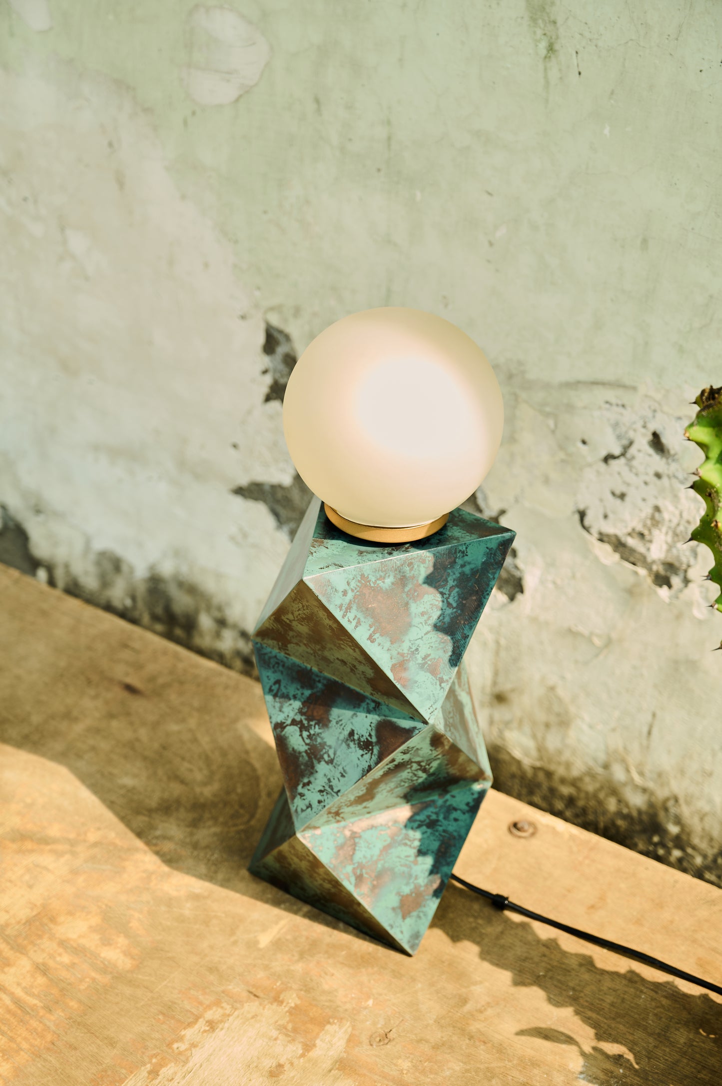 Geometric lamp with a light bulb on a wooden surface against a textured wall.