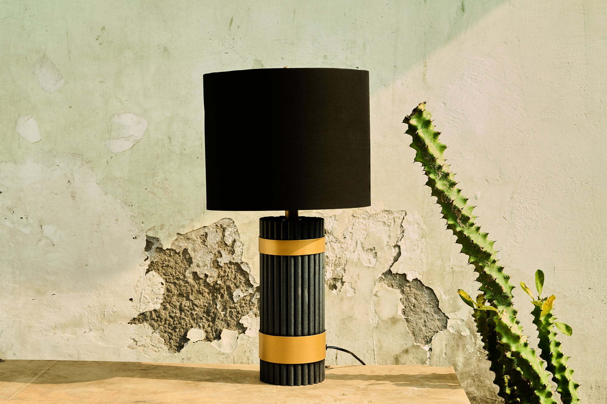 Table lamp with black and gold design on a wooden surface against a textured wall.