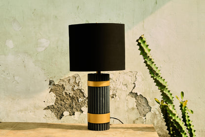 Table lamp with black and gold design on a wooden surface against a textured wall.
