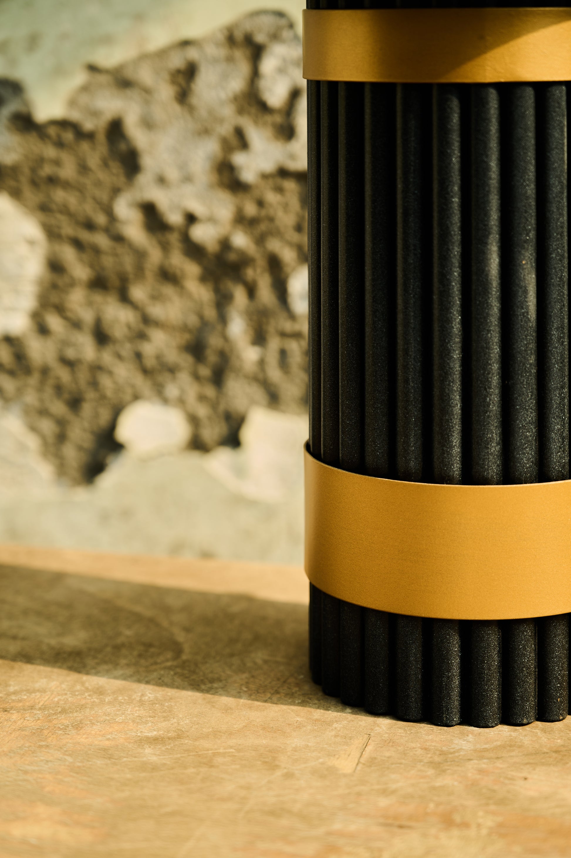 Black and gold cylindrical object on a wooden surface with a stone wall background
