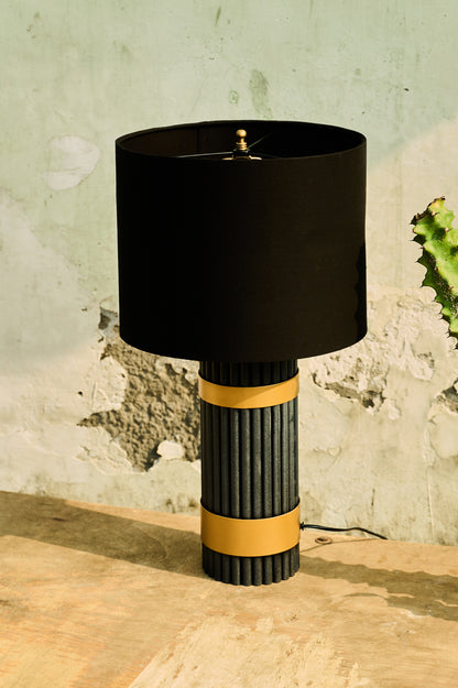 Table lamp with black shade and ribbed cylindrical base on a wooden surface.