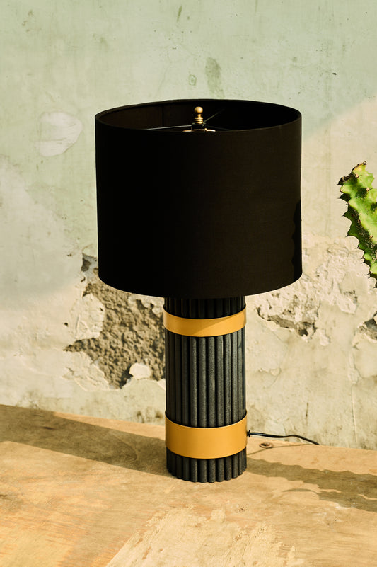 Table lamp with black shade and ribbed cylindrical base on a wooden surface.
