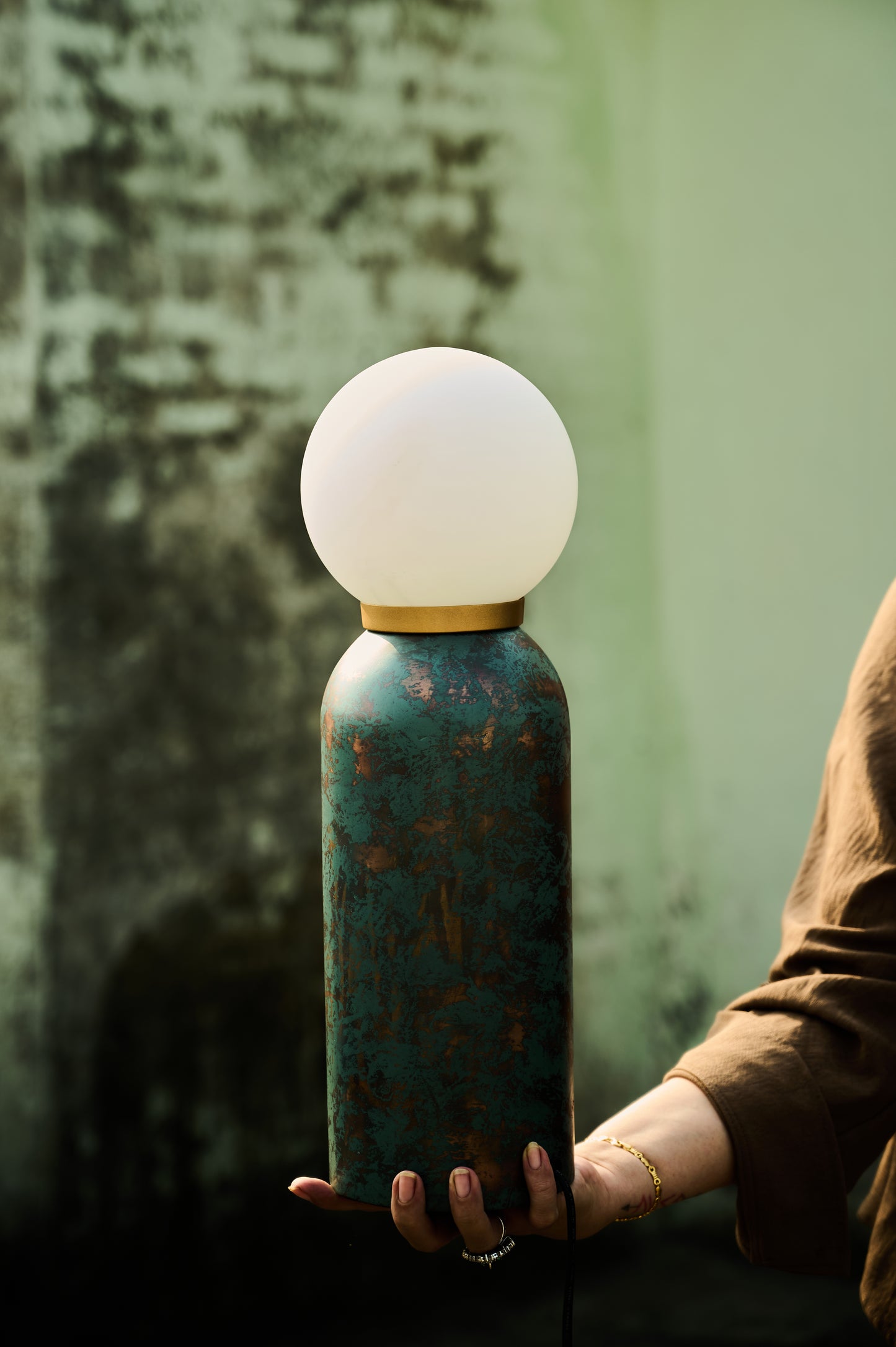 Person holding a unique lamp with a textured base and white spherical top against a blurred background