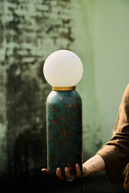 Person holding a unique lamp with a textured base and white spherical top against a blurred background