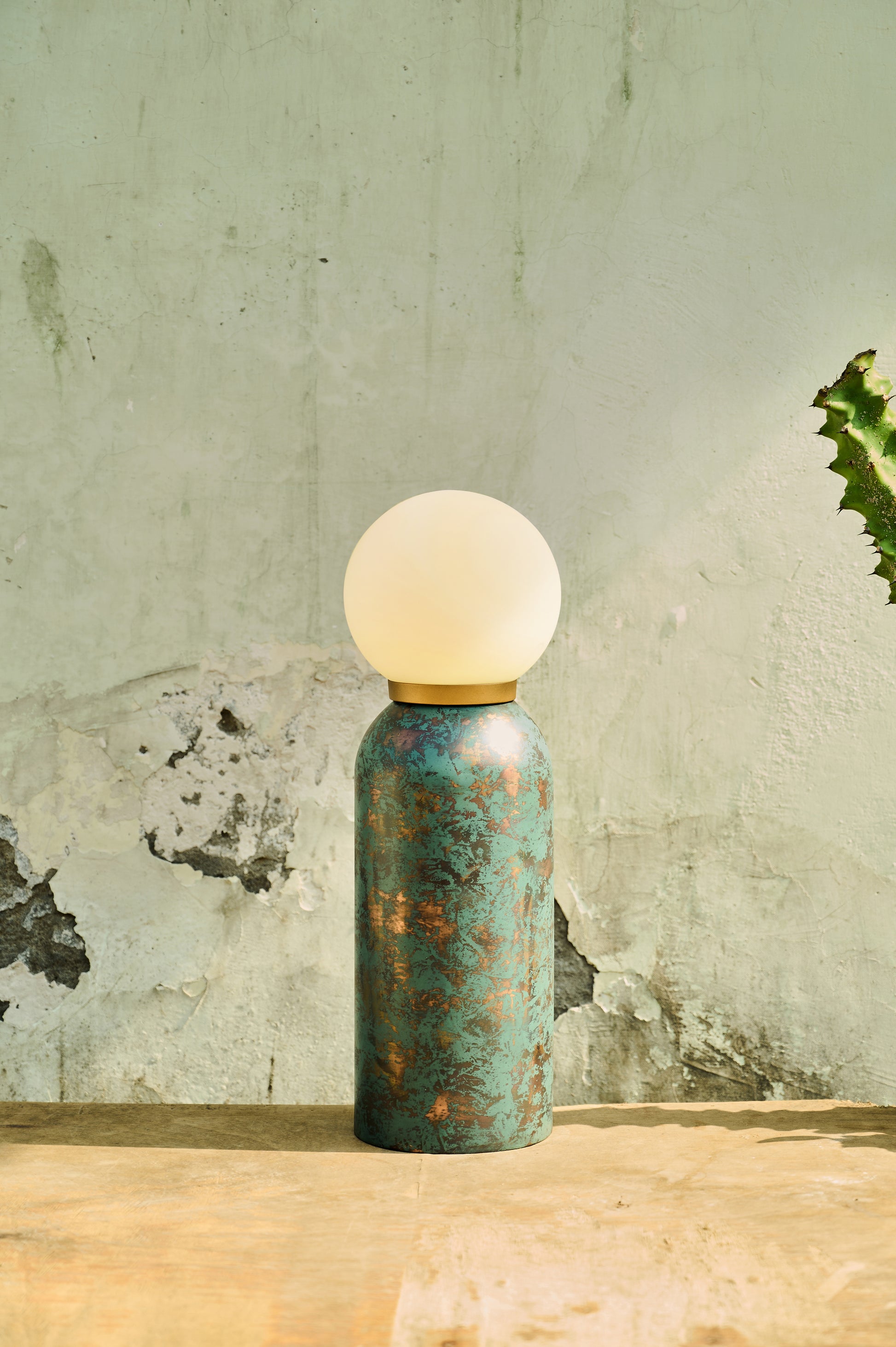 Table lamp with a textured blue base and white bulb on a wooden surface with a light green wall background.