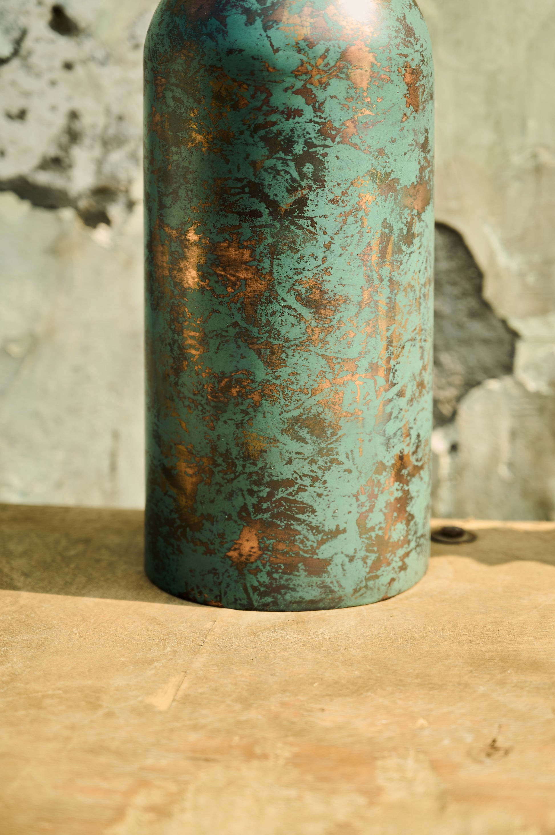 Rustic metal vase with a textured surface on a wooden surface.