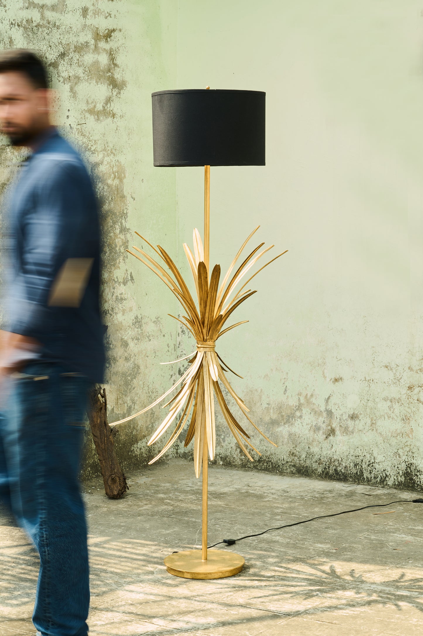 Floor lamp with decorative base and black shade in front of a textured wall.