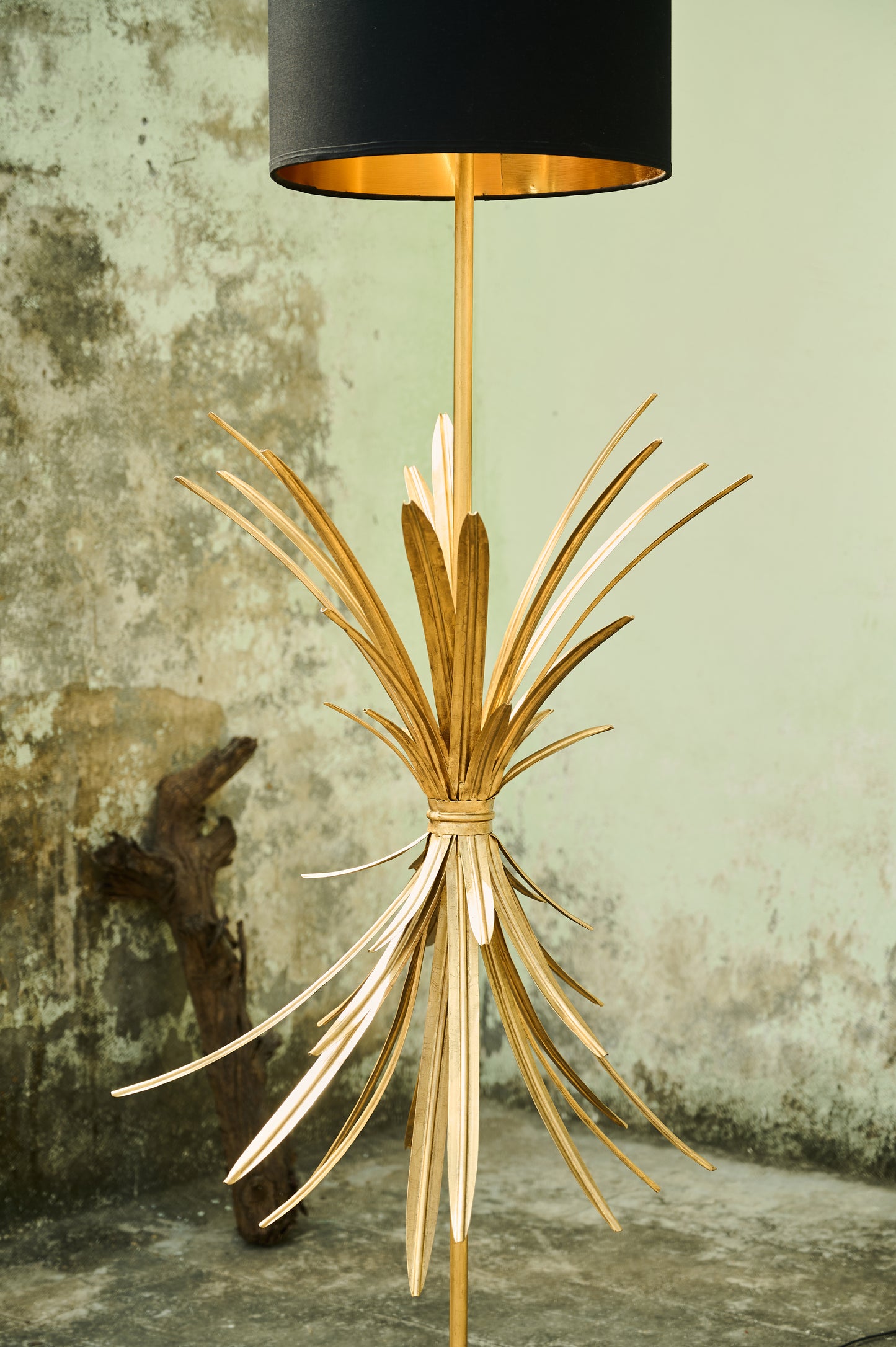 Gold floor lamp with black shade against a textured wall.