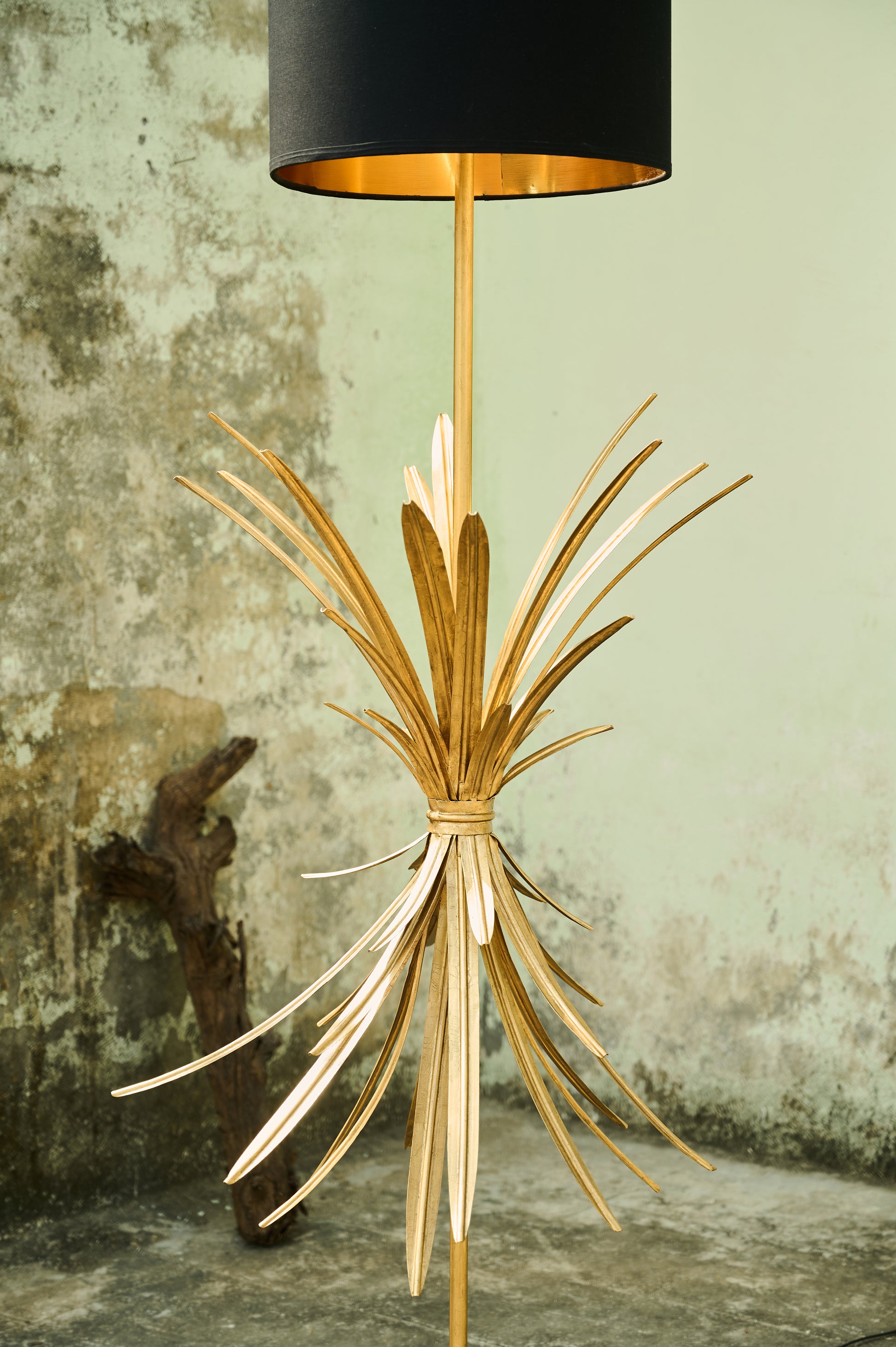 Gold floor lamp with black shade against a textured wall.
