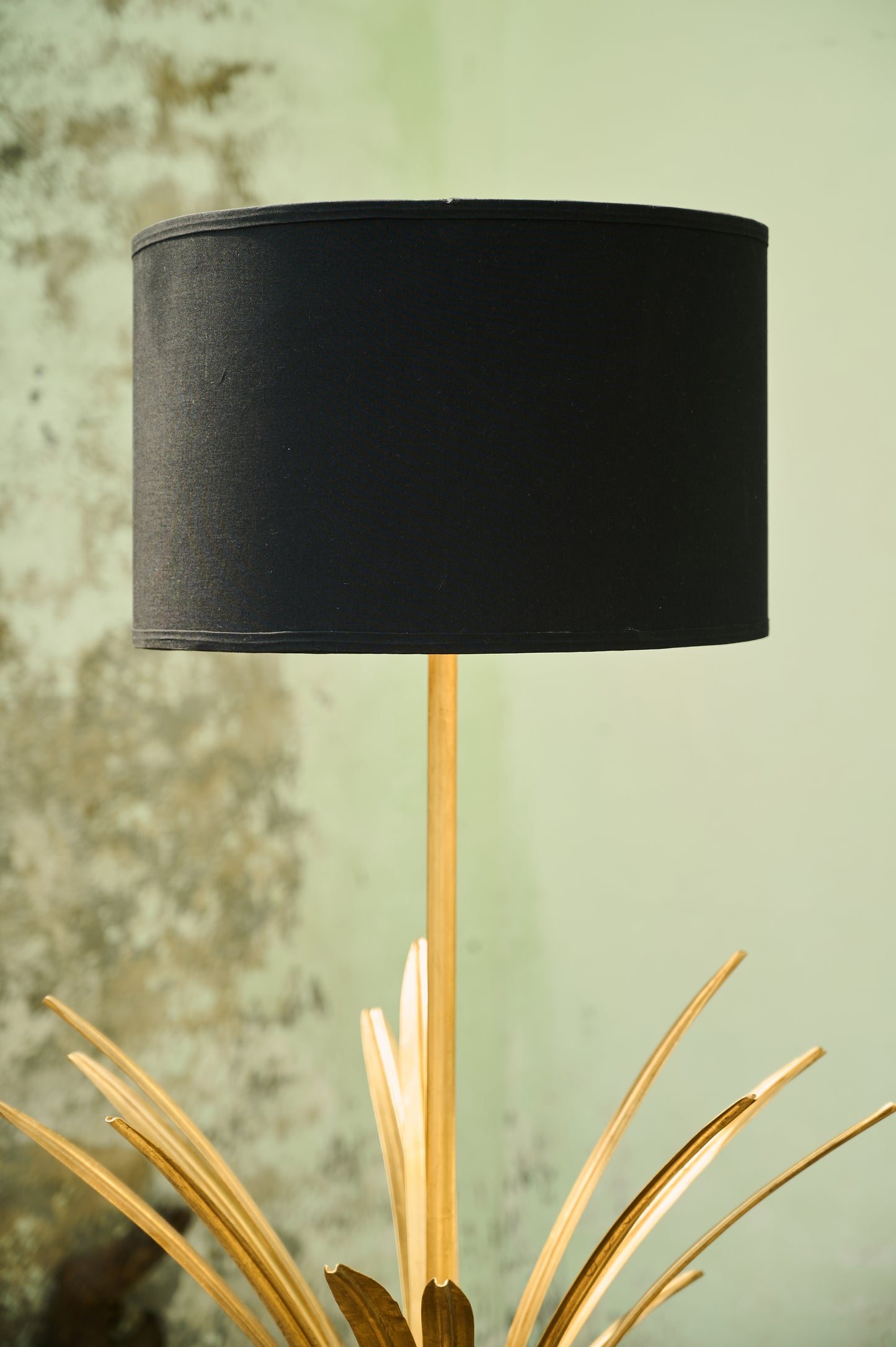Black lampshade on a decorative stand against a textured wall.