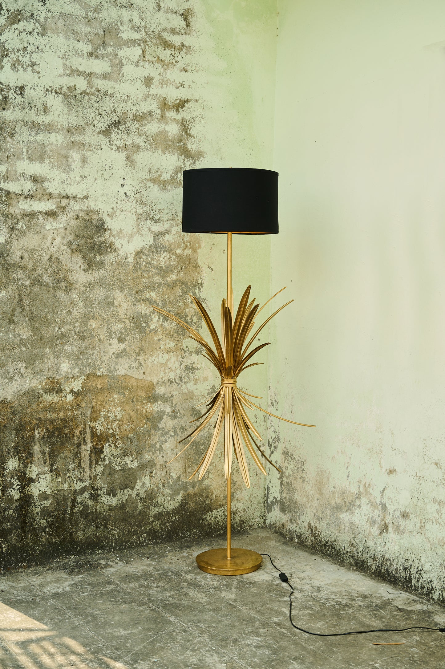Floor lamp with black shade and gold base against a textured wall.