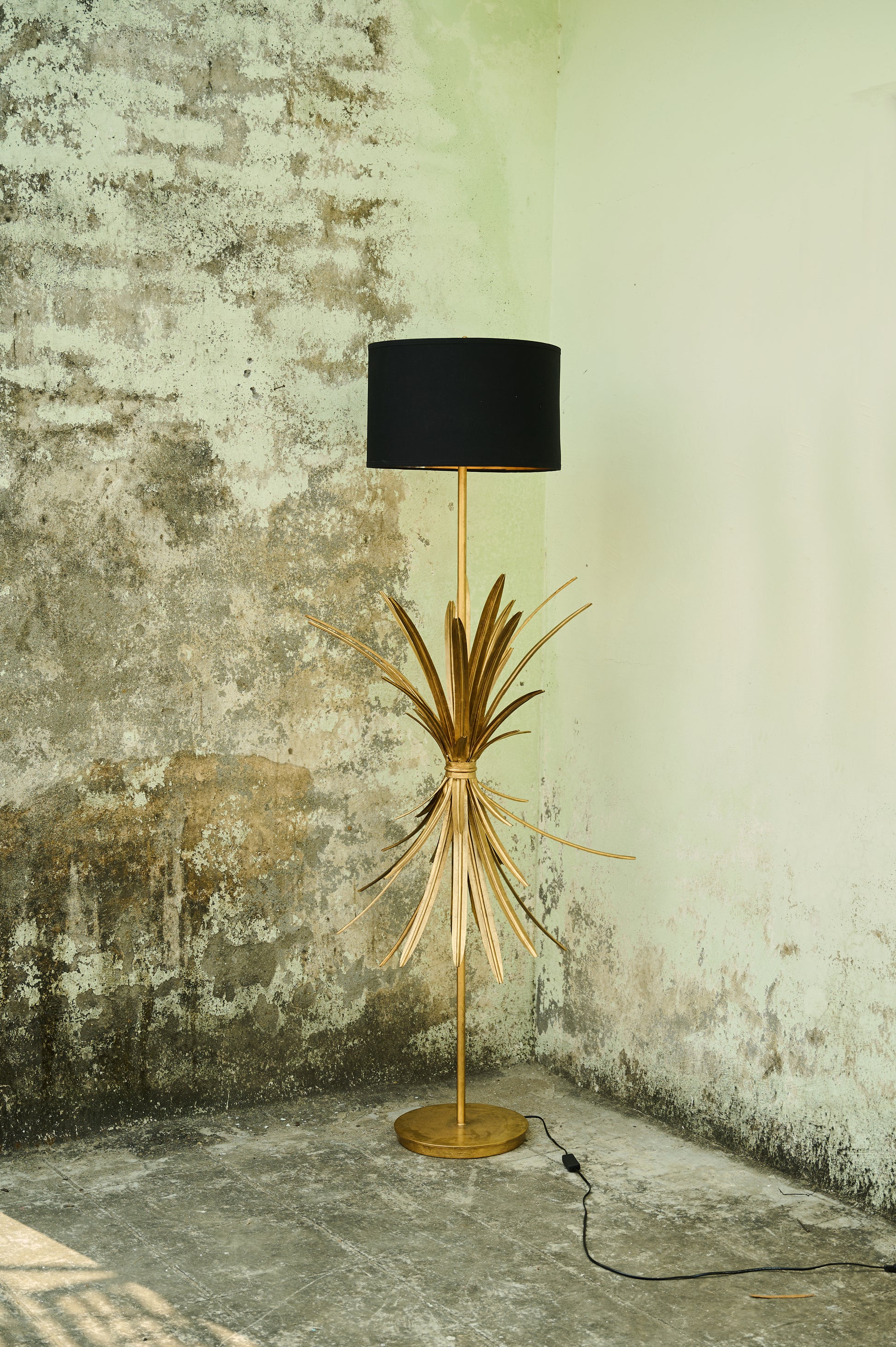 Floor lamp with black shade and gold base against a textured wall.