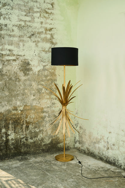 Floor lamp with black shade and gold base against a textured wall.