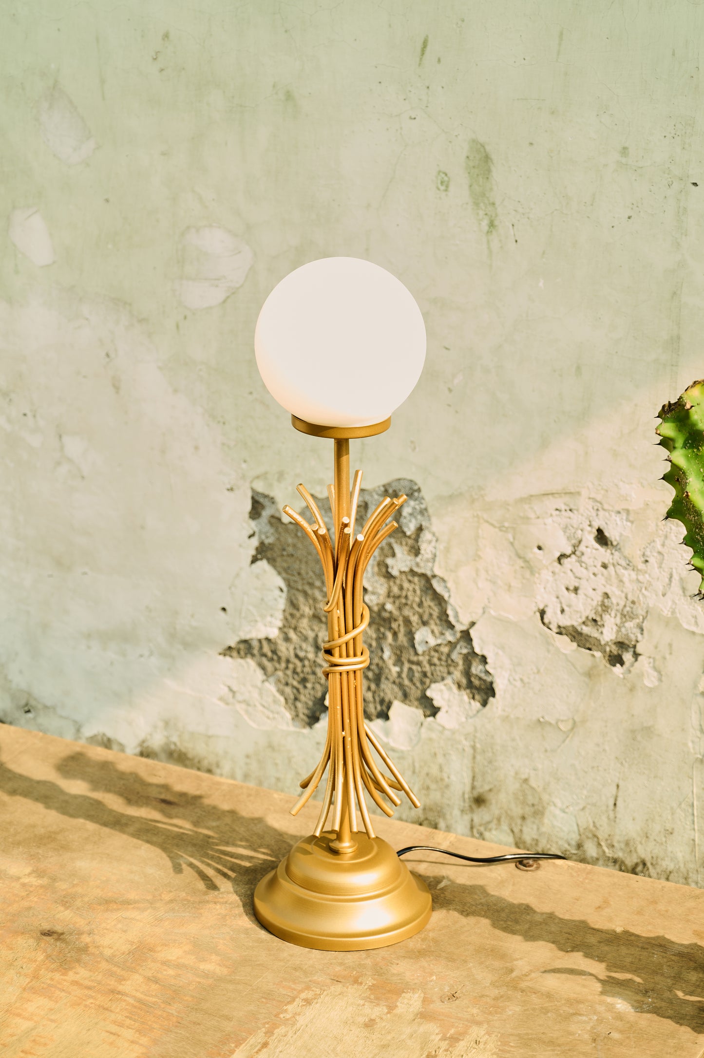 Gold table lamp with a white globe shade on a textured surface.