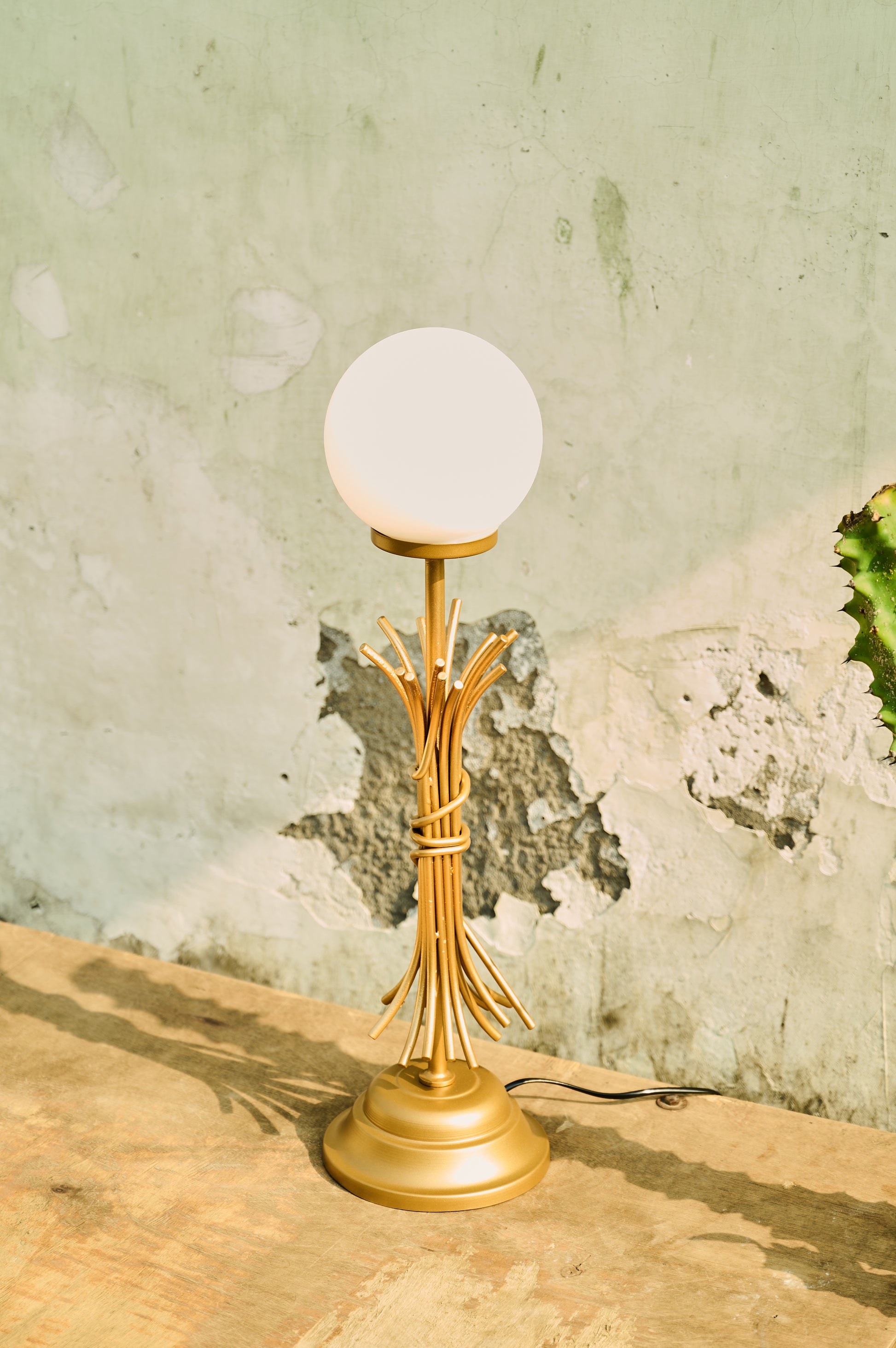 Gold table lamp with a white globe shade on a textured surface.