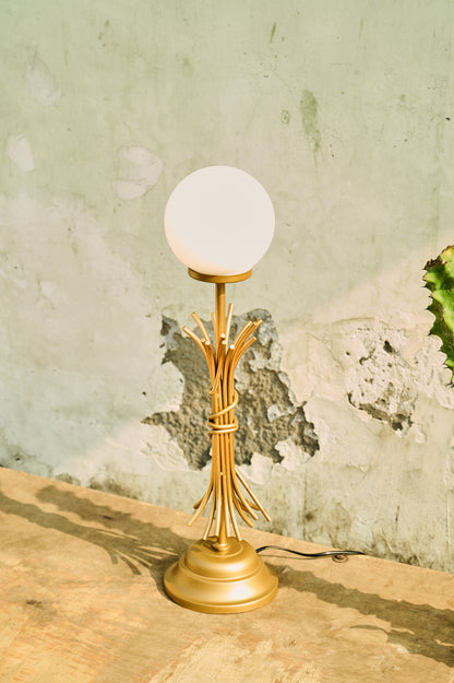 Gold table lamp with a white globe shade on a textured surface.