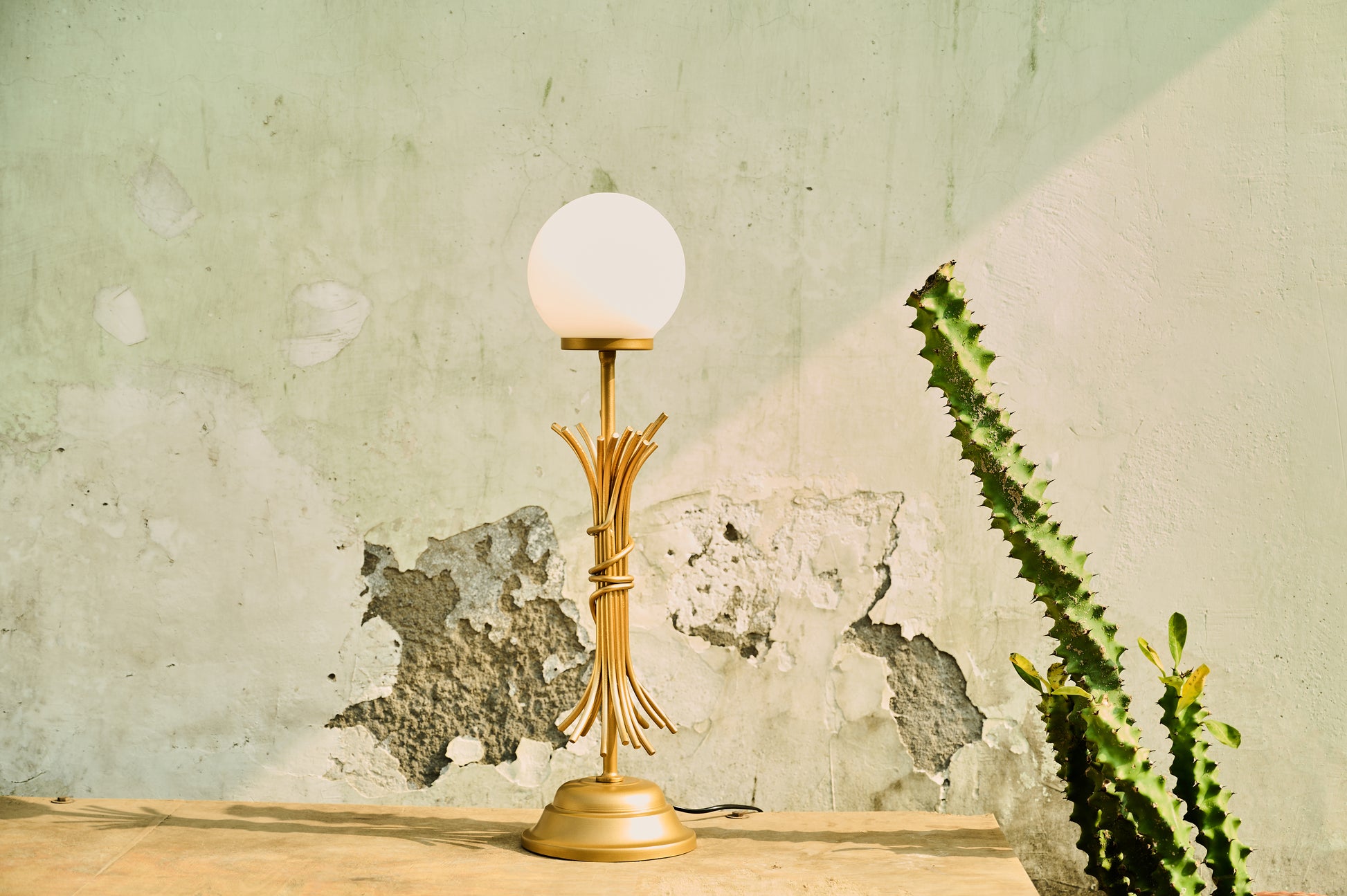 Gold table lamp with a white bulb on a wooden surface against a textured wall.