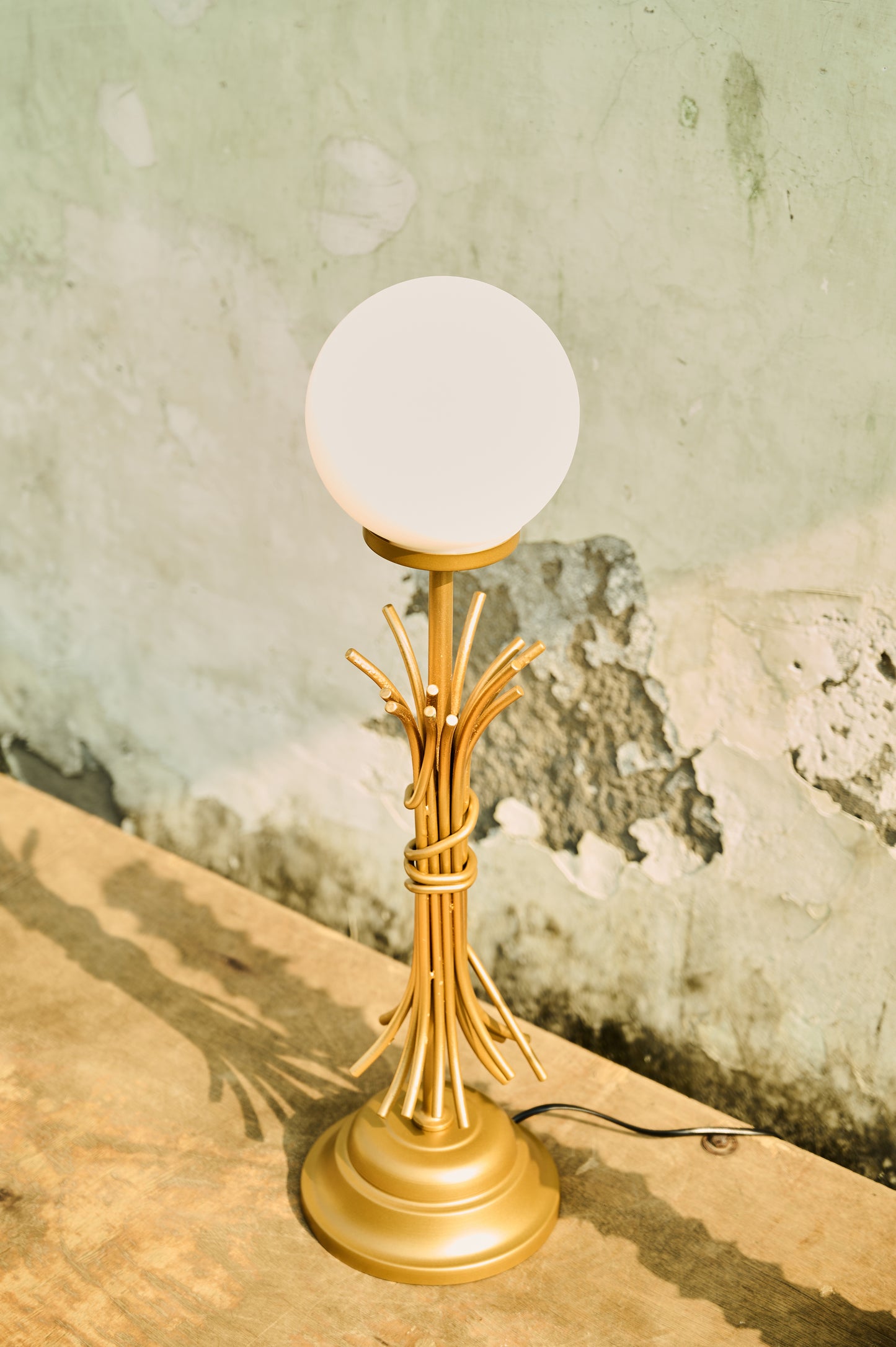 Gold table lamp with a white globe shade on a textured surface.