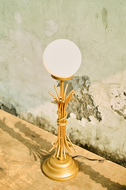 Gold table lamp with a white globe shade on a textured surface.