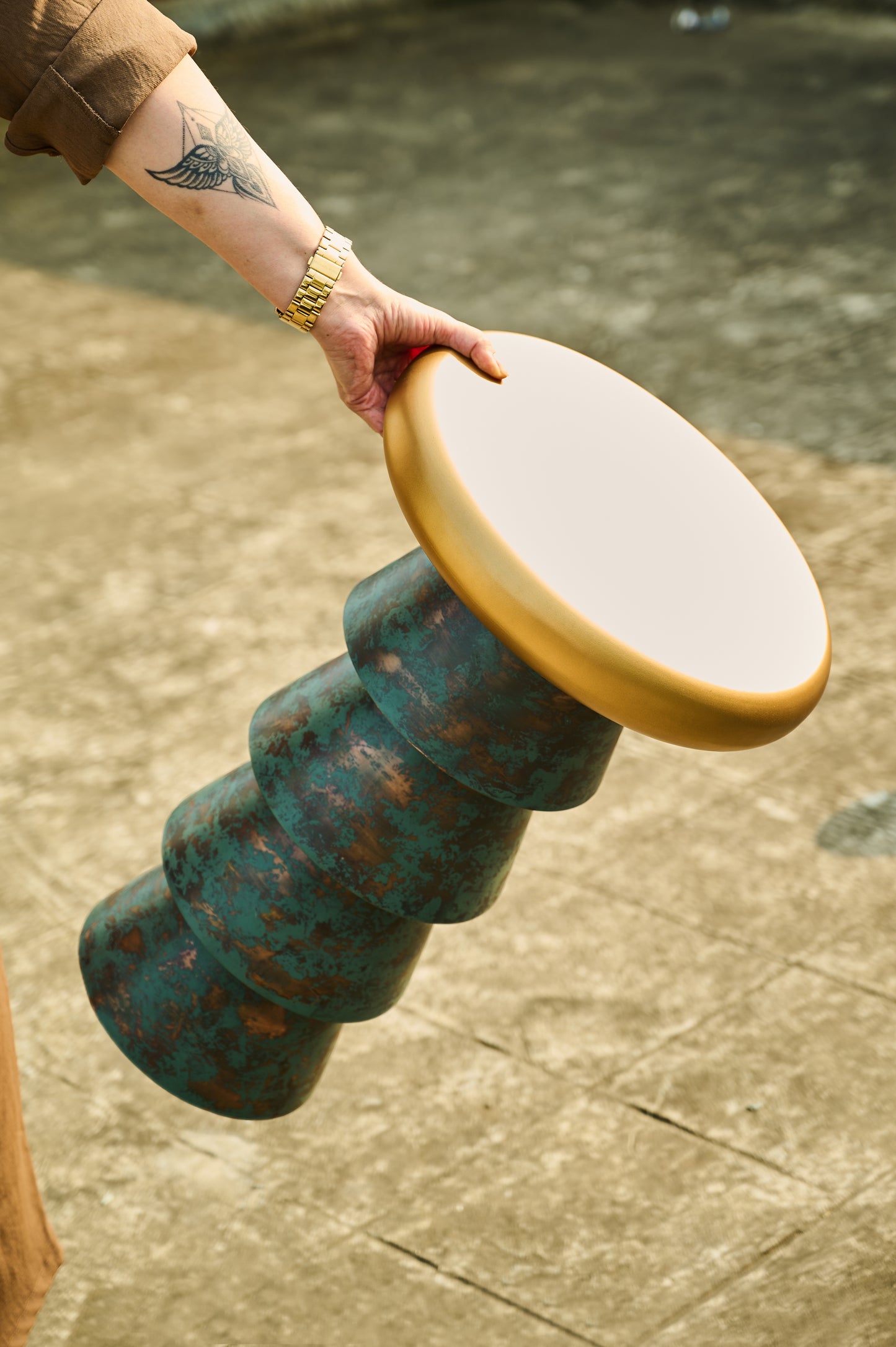 Person holding a green and gold cylindrical object on a textured surface