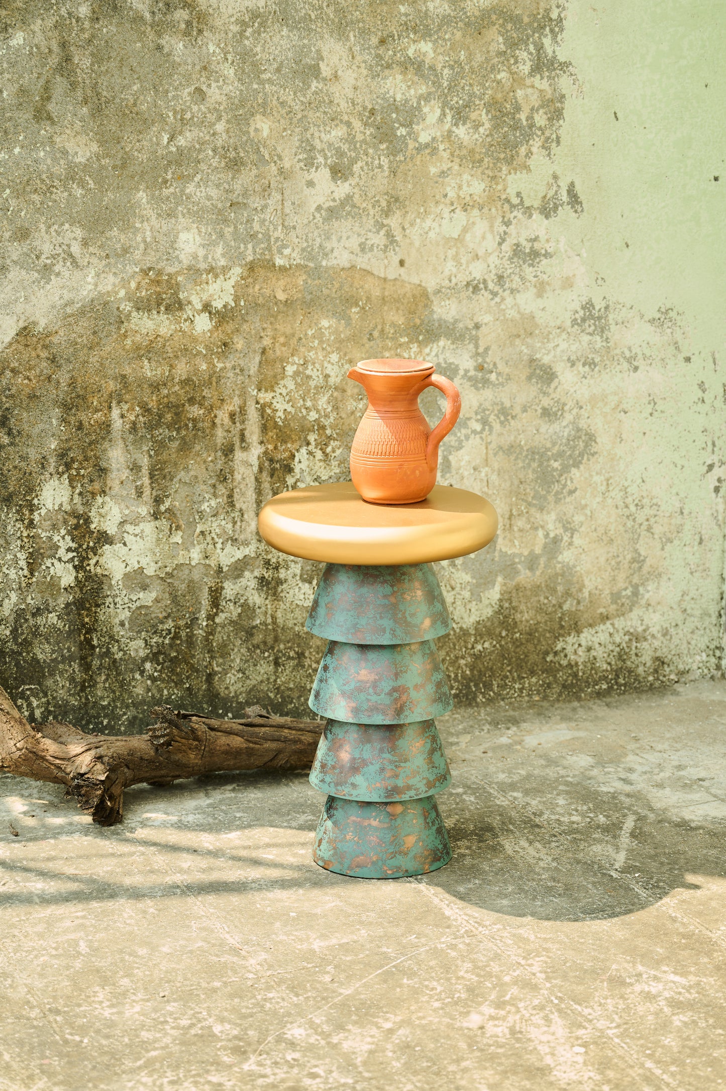 Stacked ceramic pieces with a small pitcher on top against a textured wall.