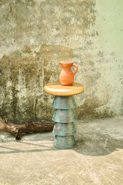 Stacked ceramic pieces with a small pitcher on top against a textured wall.