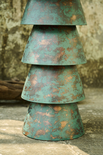Rustic, tiered metal sculpture with a textured surface on a stone surface.