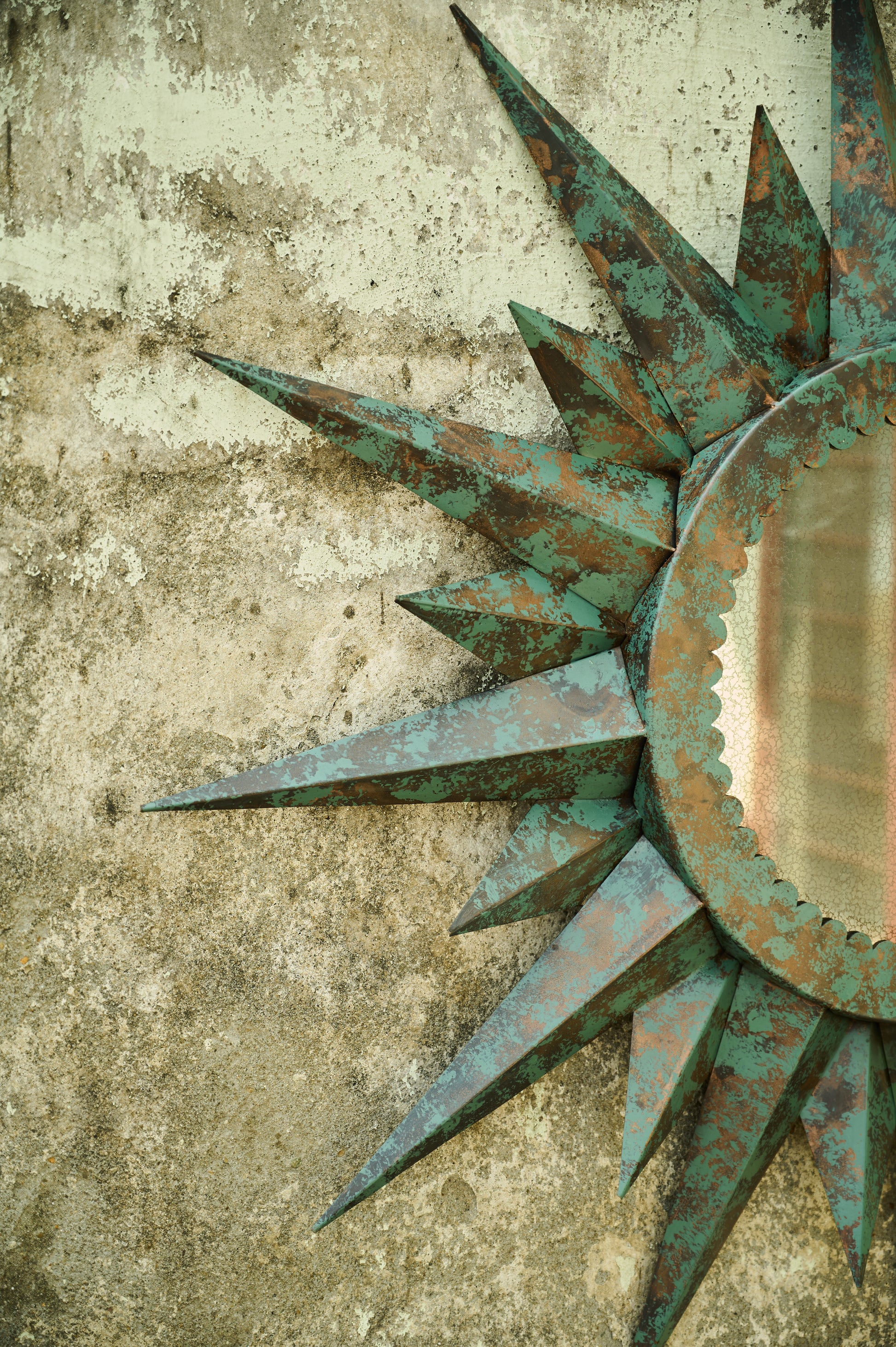 Decorative sun-shaped mirror with a textured surface on a concrete wall.