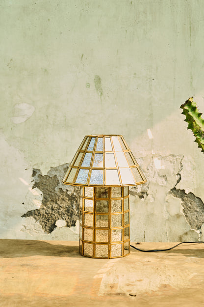 Table lamp with a decorative glass shade on a wooden surface against a textured wall.