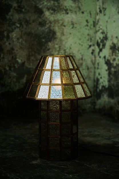 Decorative lamp with stained glass shade against a textured wall.