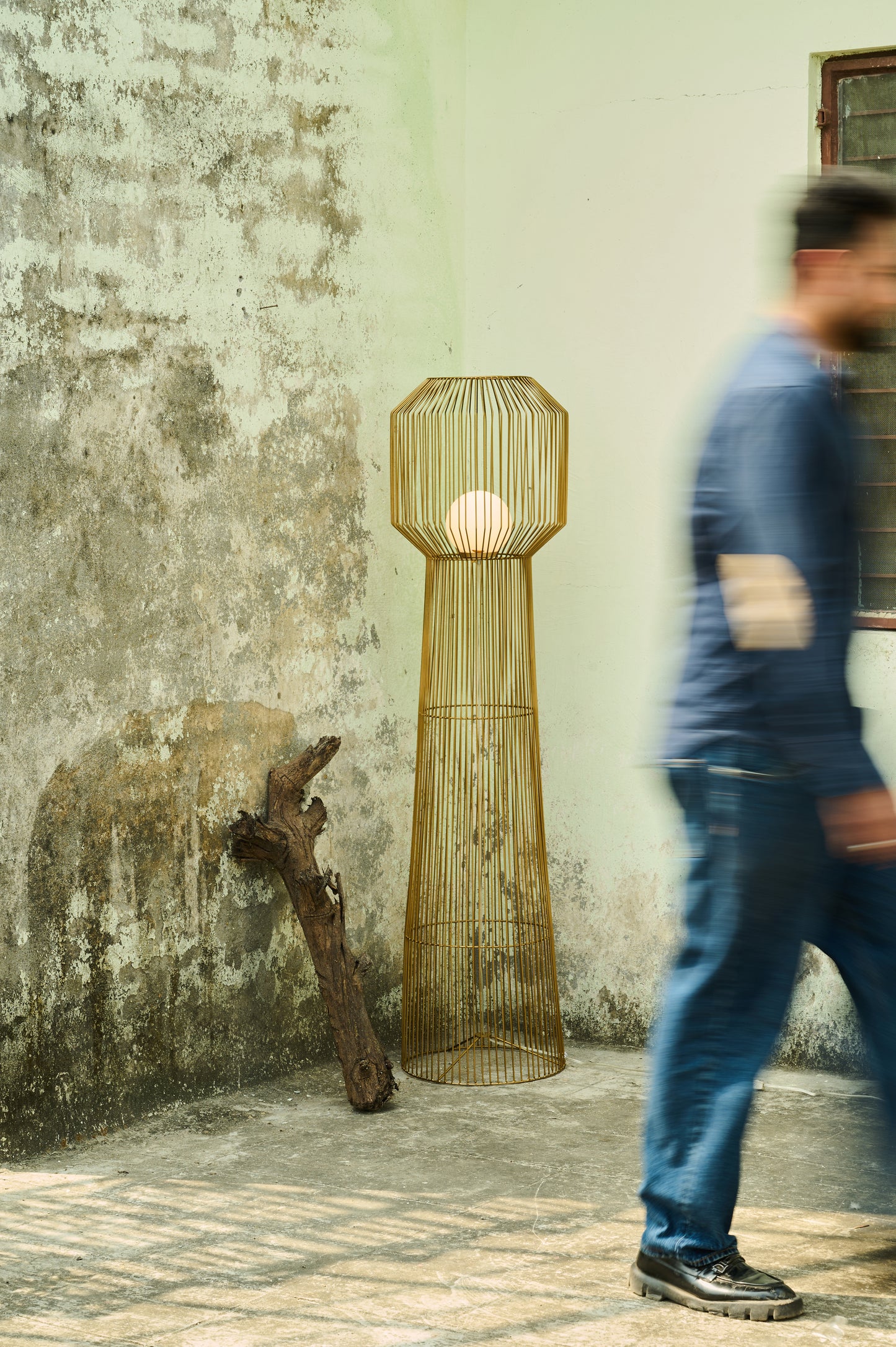 Tall woven floor lamp against a textured wall with a person walking by