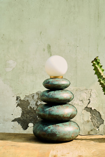 Decorative lamp with stacked stone-like bases against a textured wall.