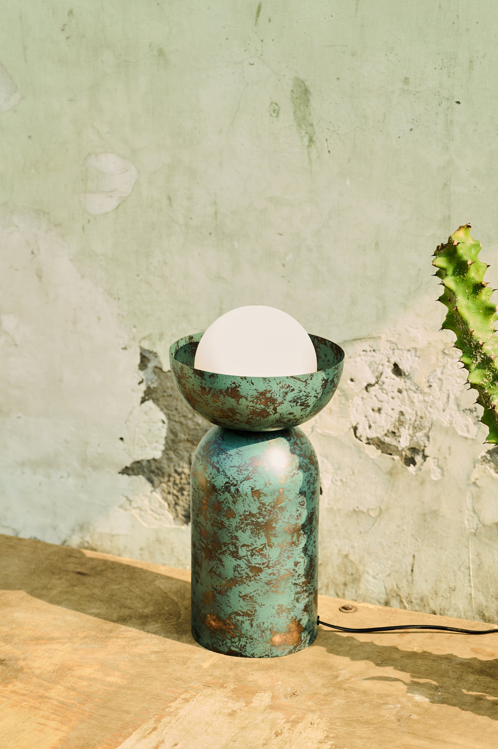 Decorative lamp with a textured green base and white shade against a textured wall.